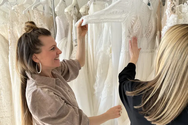 Andrea und eine Kundin suchen an der Kleiderstange ein Kleid aus