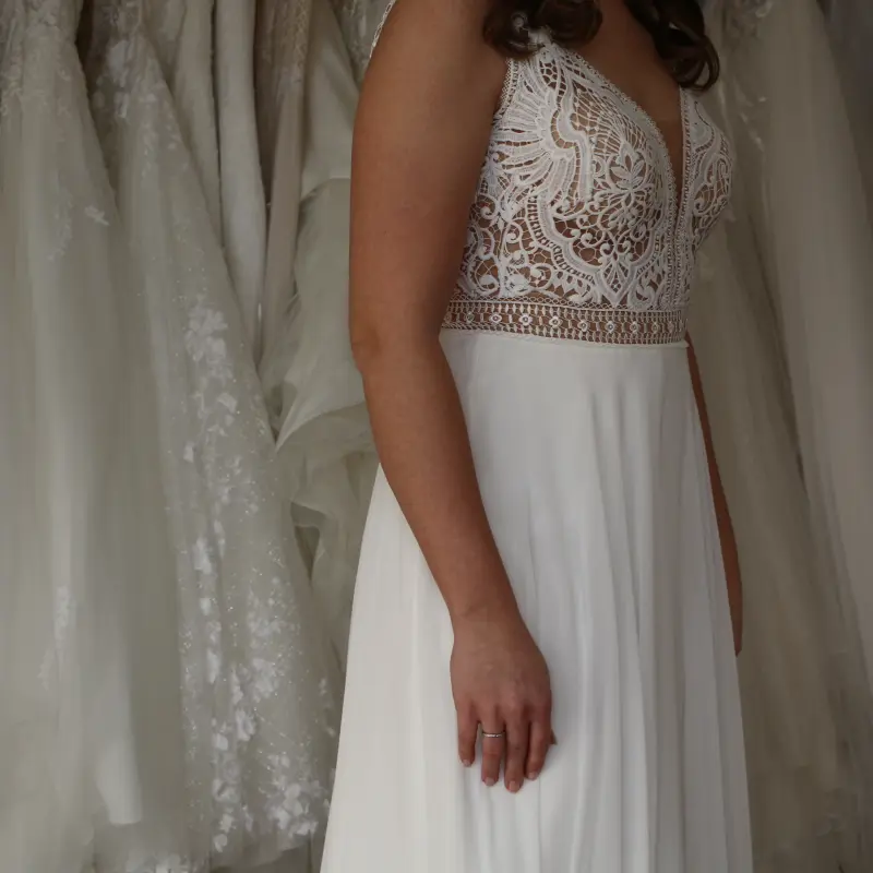 Braut im Spitzenkleid neben einer Kleiderstange voller Brautkleider im Studio